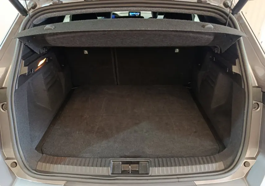 Coffre ouvert vu de l'arrière d'une Renault SYMBIOZ hybride 2025 couleur gris clair, avec tapis noir et éclairage intérieur.