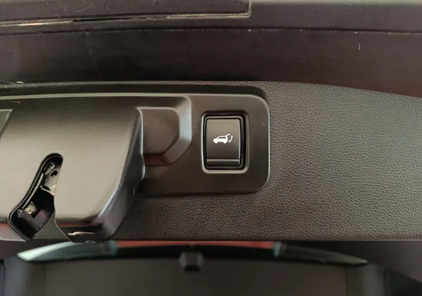 Bouton d'ouverture électrique du coffre sur panneau intérieur noir, détail du Renault SYMBIOZ hybride 2025.