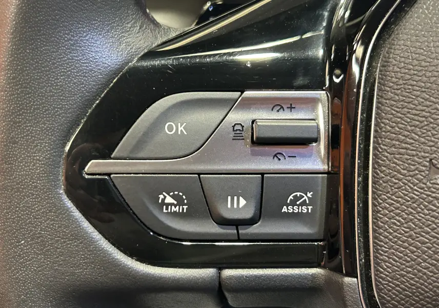 Gros plan sur les commandes noires du volant côté gauche de la Peugeot 308 gris, avec boutons de régulateur et limiteur de vitesse.