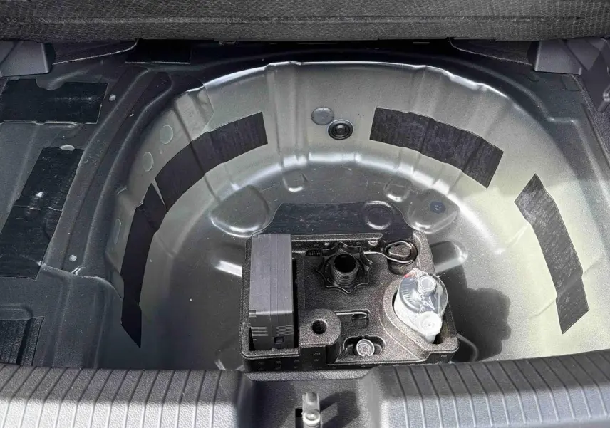 Coffre ouvert vu de dessus montrant le rangement sous plancher avec kit de dépannage sur Volkswagen Polo noire 2025.