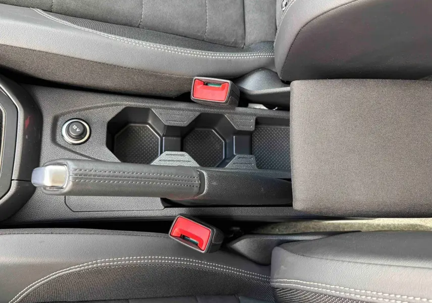 Vue plongeante sur la console centrale noire de la Volkswagen Polo 2025, avec frein à main manuel et porte-gobelets.
