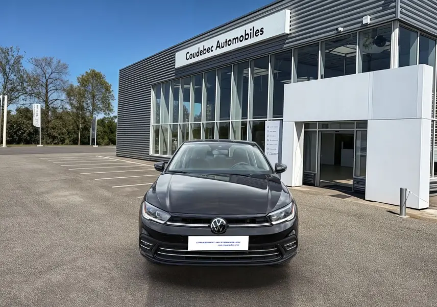 Vue avant d'une Volkswagen Polo noire 2025 stationnée devant un bâtiment moderne de concession automobile.