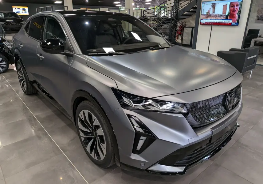 Renault Rafale E-Tech gris schiste satin en 3/4 avant droit, avec calandre noire à motif losange et phares LED fins.