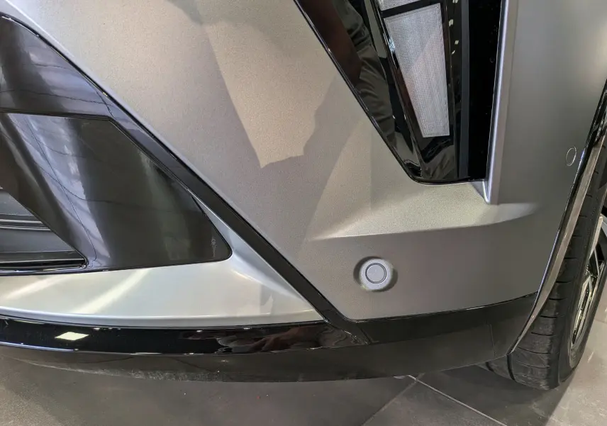 Gros plan sur le pare-chocs avant droit gris schiste satin de la Renault Rafale E-Tech avec capteur de stationnement visible.