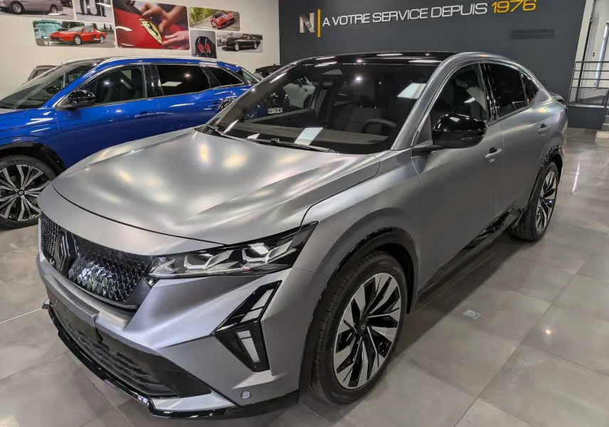Renault Rafale E-Tech gris schiste satin en 3/4 avant droit, avec calandre noire et jantes bicolores en showroom.
