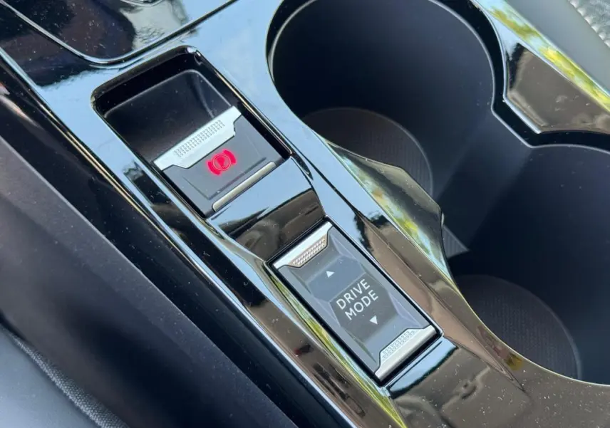 Gros plan sur la console centrale noire de la Peugeot 208 Hybrid 110 e-DCS6 Allure avec bouton frein à main électrique et mode de conduite.