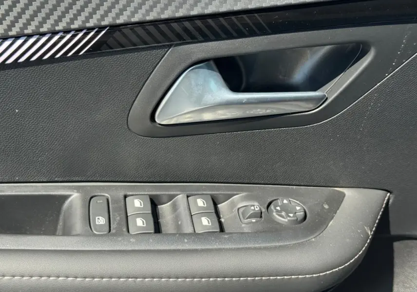 Gros plan sur la poignée intérieure et les commandes des vitres électriques côté conducteur d’une Peugeot 208 gris 2025.