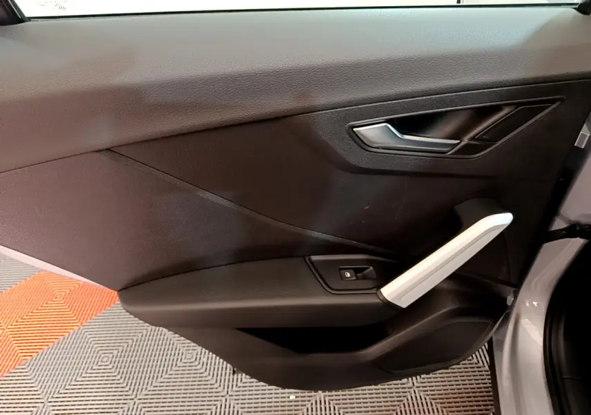 Vue rapprochée de la porte avant droite de l'Audi Q2 gris clair, avec poignée argentée et bouton de verrouillage.