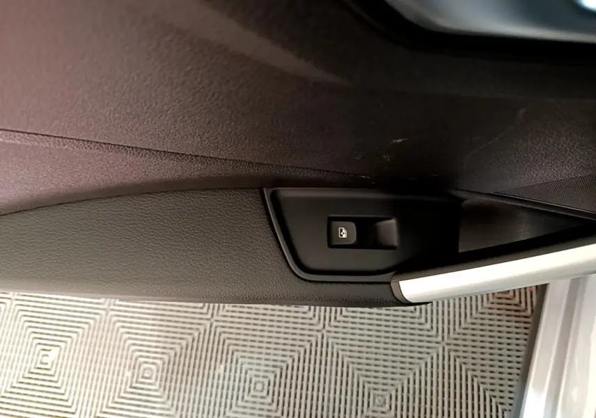 Détail de la commande d'ouverture du coffre sur la porte intérieure d'un Audi Q2 gris clair, vue rapprochée.