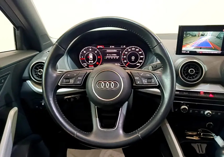 Vue intérieure centrée sur le volant cuir multifonctions d’un Audi Q2 35 TDI 150 Design avec tableau de bord digital.