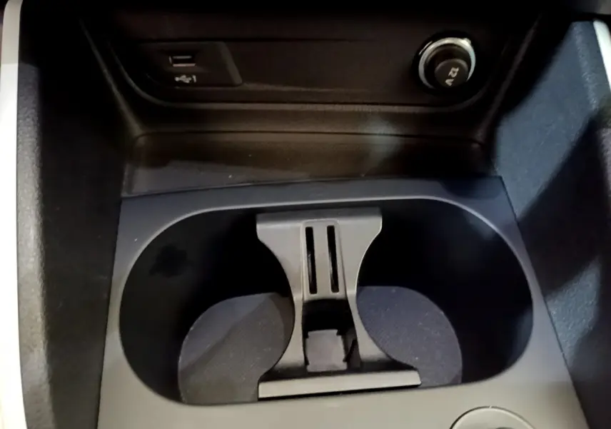 Gros plan sur les porte-gobelets centraux noirs de l’Audi Q2 35 TDI 150 Design gris clair, avec prise 12V visible.