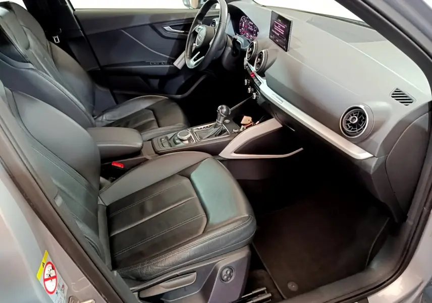 Vue intérieure côté conducteur de l'Audi Q2 gris clair 2020, sièges cuir noirs et tableau de bord moderne avec écran central.