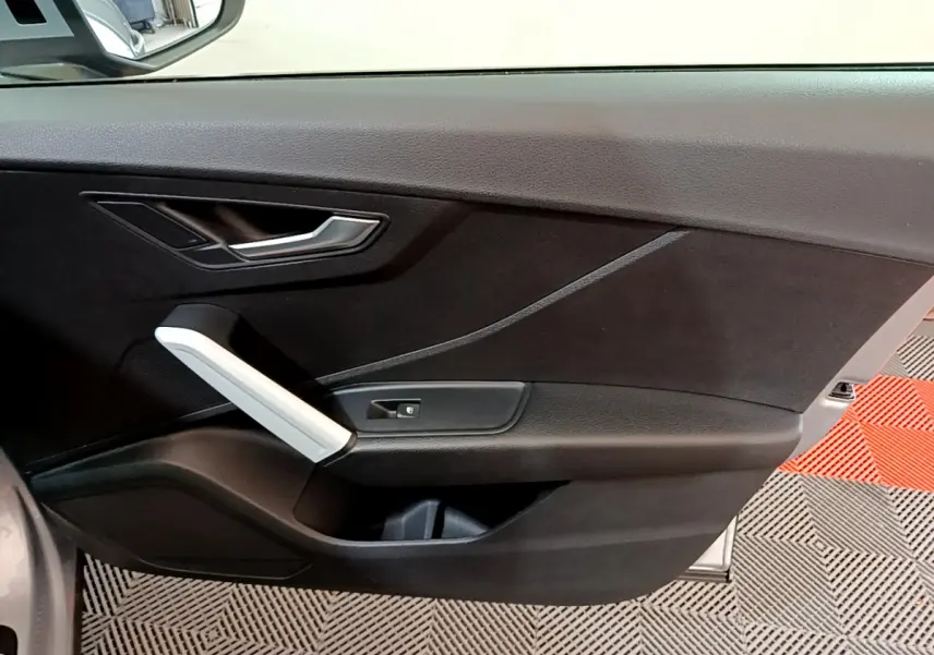 Vue intérieure du panneau de porte côté conducteur d'un Audi Q2 gris clair, avec poignée argentée et bouton de verrouillage.