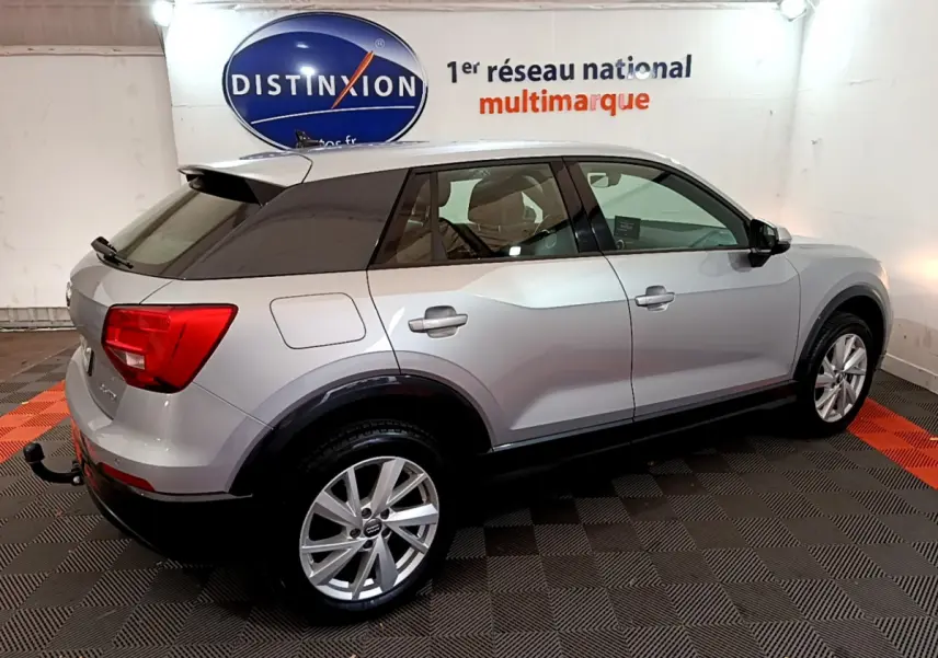 Audi Q2 gris clair vue de côté droit arrière, avec toit noir et feux arrière rouges en intérieur showroom.