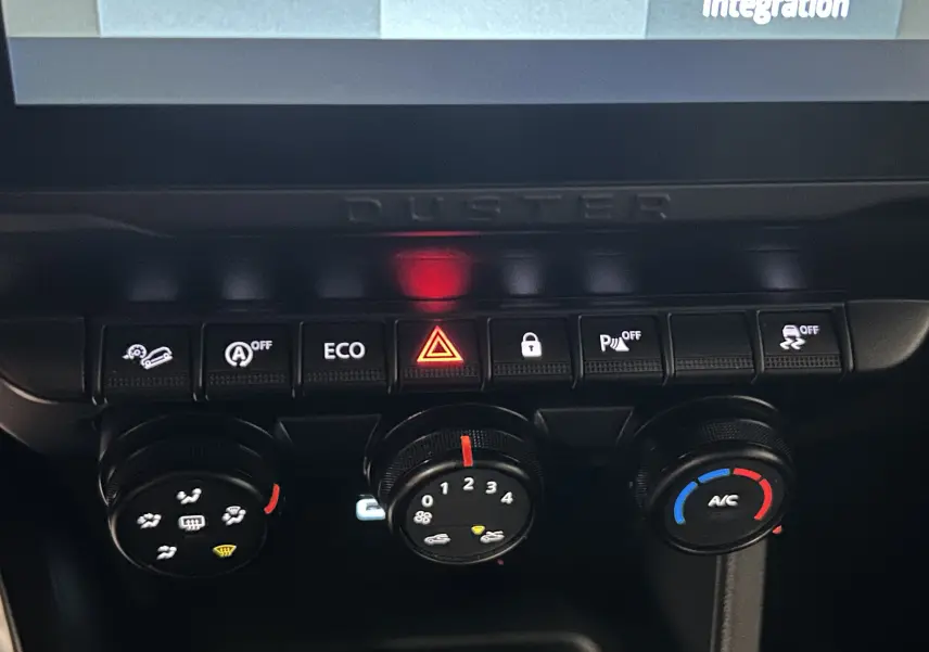 Gros plan sur la console centrale du Dacia Duster 2024, montrant les commandes climatiques et boutons de sécurité.