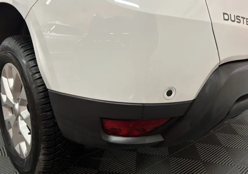 Gros plan sur l’angle arrière droit blanc du Dacia Duster 2024, avec feu arrière et capteur de recul visibles.