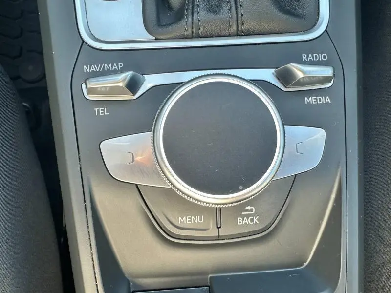 Gros plan sur la molette de commande multimédia argentée dans la console centrale noire de l'Audi Q2 blanche.