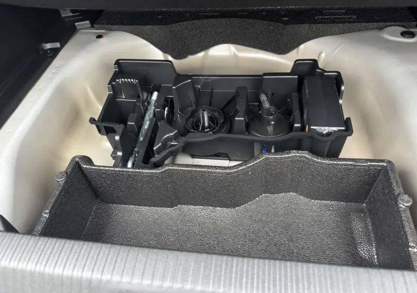 Coffre ouvert du Peugeot 2008 hybride 2025 montrant le rangement sous plancher avec outils et espace de rangement noir.