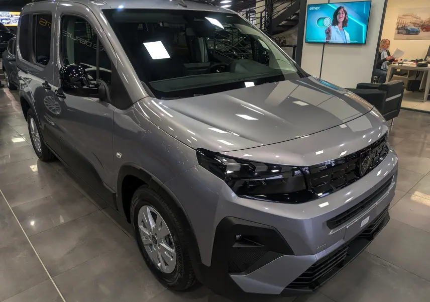 Peugeot Rifter gris acier vu en 3/4 avant droit, avec calandre noire brillante et jantes acier en showroom.