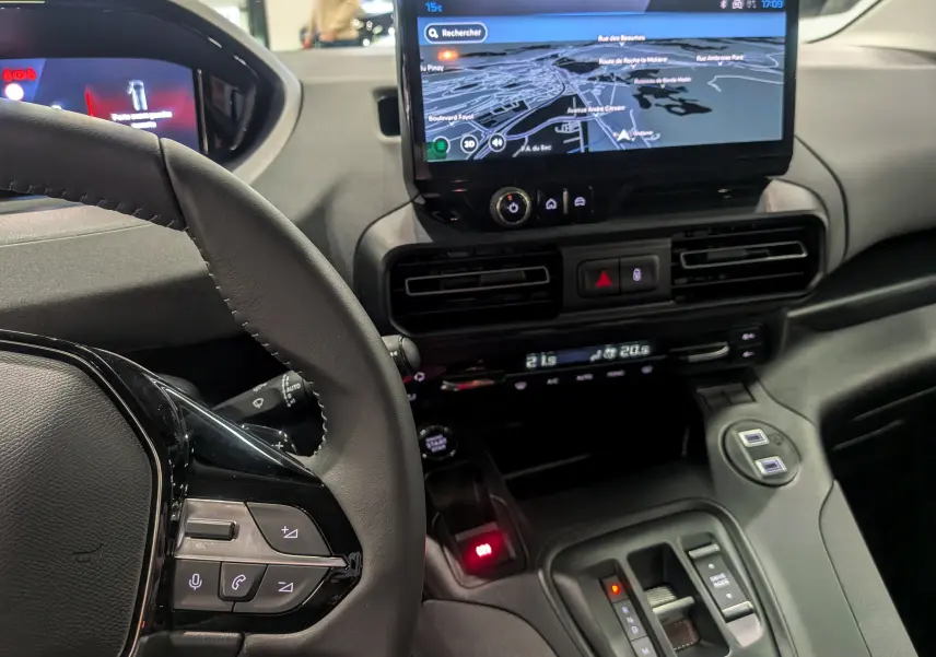 Vue intérieure centrée sur le tableau de bord et le volant du Peugeot Rifter gris acier, avec écran tactile affichant la navigation.