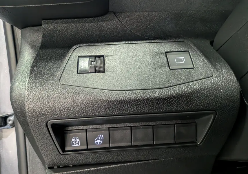 Gros plan sur les commandes noires du tableau de bord côté gauche du Peugeot Rifter gris acier 2025, avec boutons chauffant volant et sécurité enfant.