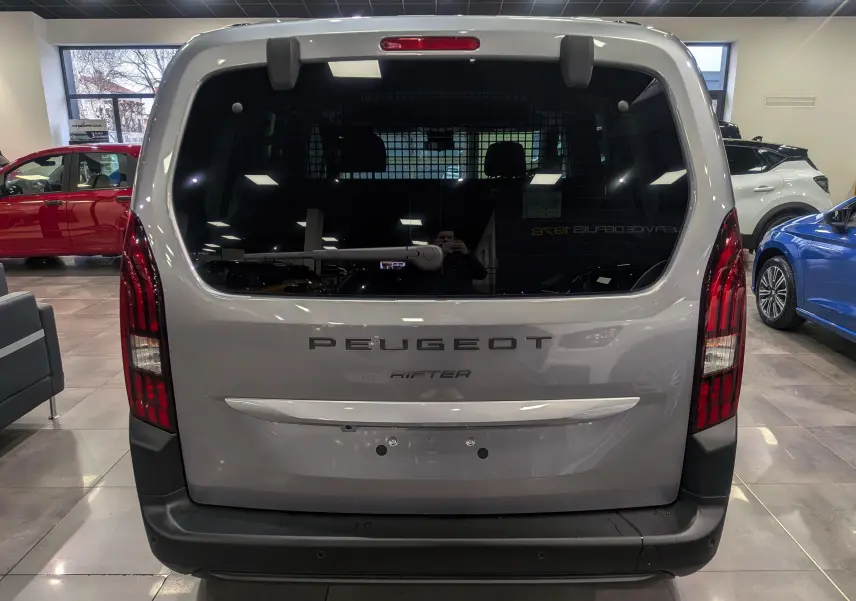 Vue arrière d'un Peugeot Rifter gris acier 2025 avec hayon vitré et feux verticaux rouges en concession.