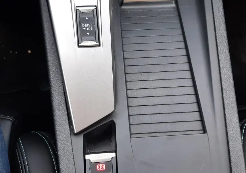 Vue rapprochée de la console centrale noire et grise du Peugeot 408 Hybrid 2024 avec bouton Drive Mode et frein à main électronique.