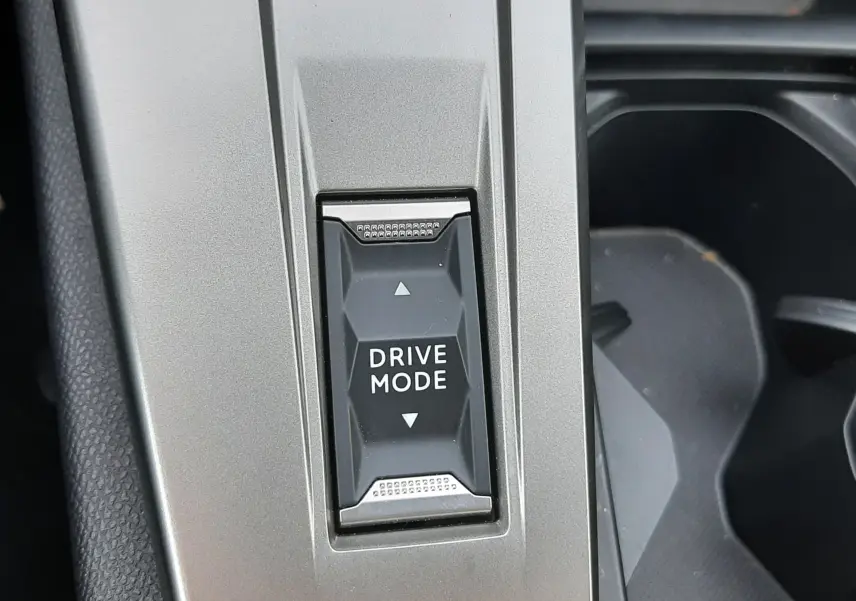 Gros plan sur le bouton Drive Mode intégré dans la console centrale gris sélénium de la Peugeot 408 Hybrid 2024.
