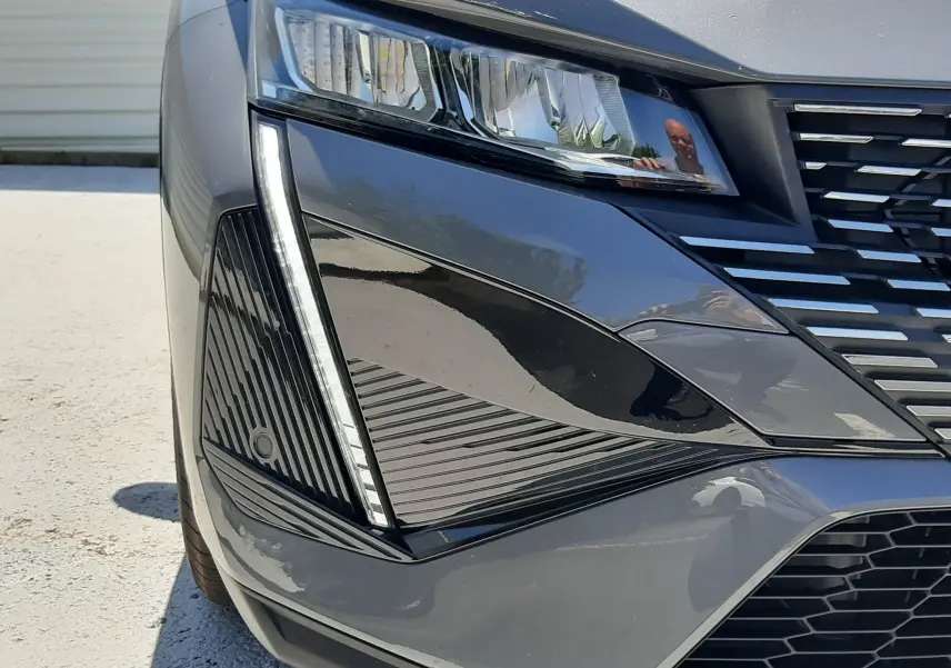 Gros plan sur le phare avant gauche gris sélénium du Peugeot 408 Hybrid 145ch avec détails LED et calandre noire.