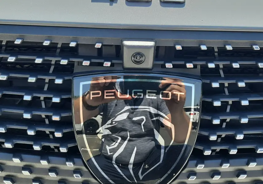 Gros plan sur la calandre gris sélénium du Peugeot 408 2024 avec logo lion et caméra frontale intégrée.