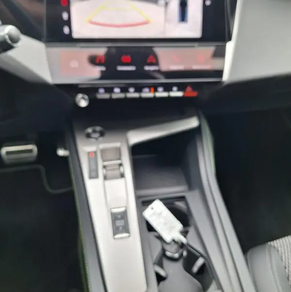 Vue intérieure centrée sur la console centrale et l'écran tactile affichant la caméra de recul du Peugeot 308 gris Hybrid 145 e-DCS6 GT.