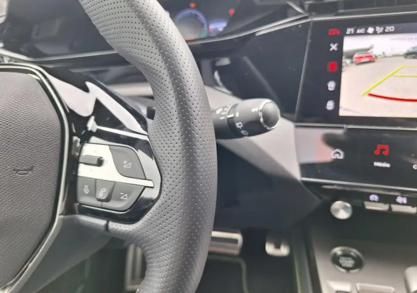 Vue intérieure rapprochée du volant perforé et de l’écran tactile affichant la caméra de recul du Peugeot 308 gris Hybrid 145 e-DCS6 GT.