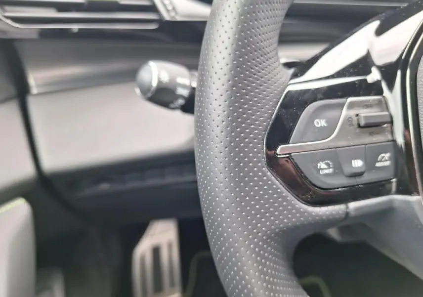 Gros plan sur le volant perforé et les commandes multifonctions du Peugeot 308 Hybrid 145 e-DCS6 GT, intérieur noir.