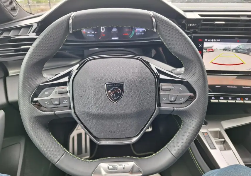 Vue intérieure centrée sur le volant gris perforé du Peugeot 308 Hybrid 145 e-DCS6 GT avec cockpit numérique et écran multimédia.