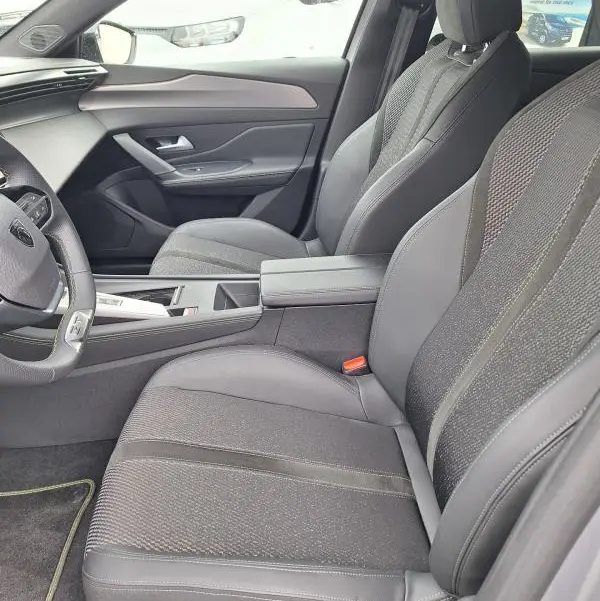 Vue intérieure côté conducteur de la Peugeot 308 Hybrid 145 e-DCS6 GT 2025 gris, sièges tissu et cuir, tableau de bord moderne.