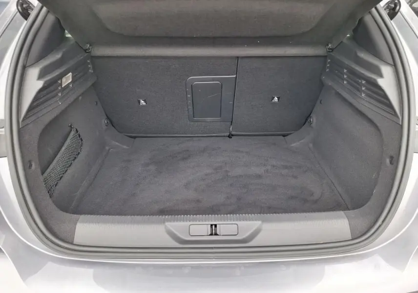 Coffre ouvert vu de l'arrière d'une Peugeot 308 Hybrid 145 gris, montrant un espace de rangement propre et spacieux.