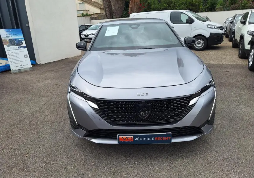 Vue avant d'une Peugeot 308 Hybrid 145 e-DCS6 GT gris métallisé avec calandre noire et feux LED fins.