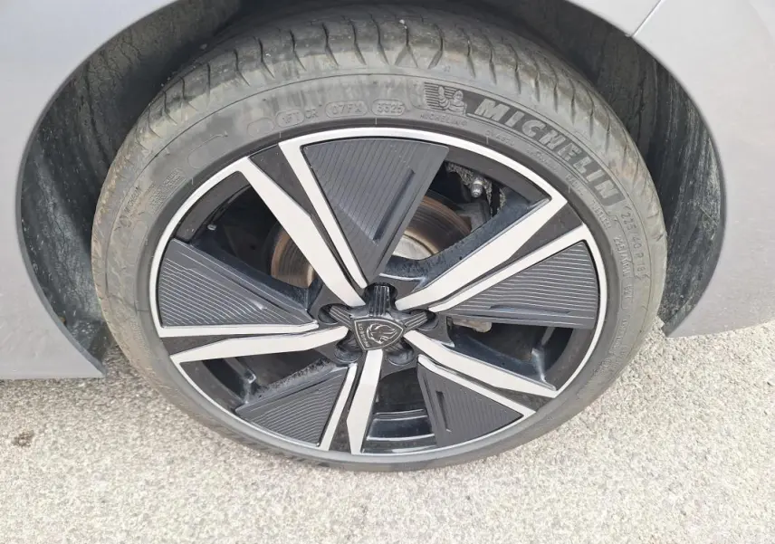 Gros plan sur la jante alliage noire et argentée de 18 pouces du Peugeot 308 Hybrid 145 e-DCS6 GT gris, côté droit.