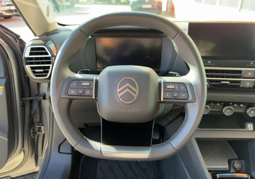 Vue centrée sur le volant cuir et tableau de bord numérique du Citroën C4 hybride 2025, intérieur gris.