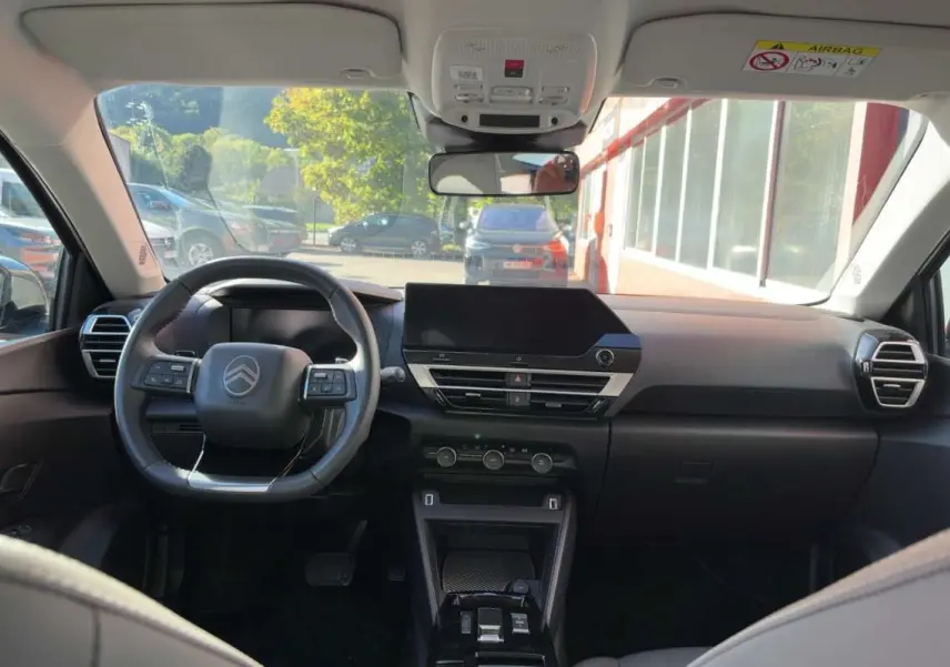 Vue intérieure avant du Citroën C4 hybride 2025, tableau de bord noir avec volant cuir et écran tactile central.