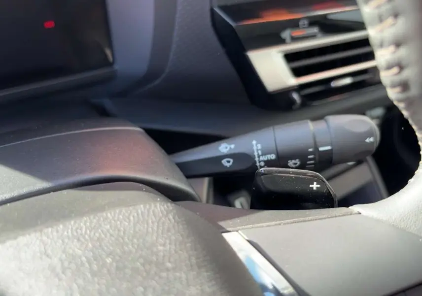 Détail intérieur du volant cuir de la Citroën C4 hybride 2025, avec palette de changement de vitesse et commande d’essuie-glace.