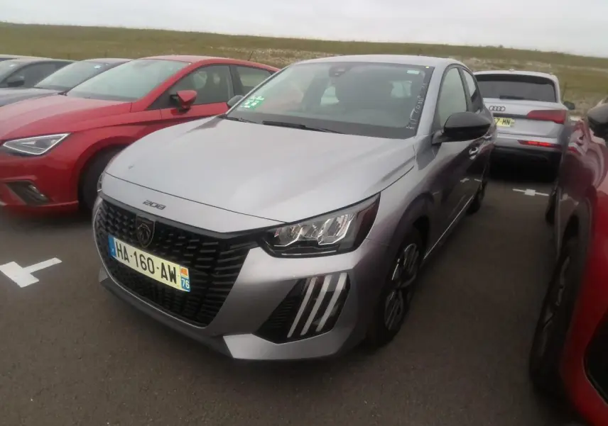 Peugeot 208 gris clair vue 3/4 avant droit, avec calandre noire et feux avant distinctifs en forme de griffes.