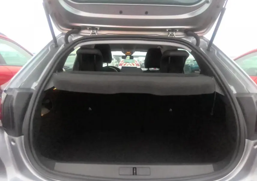 Coffre ouvert vu de l'arrière d'une Peugeot 208 gris clair 2024, montrant l'espace de chargement vide.