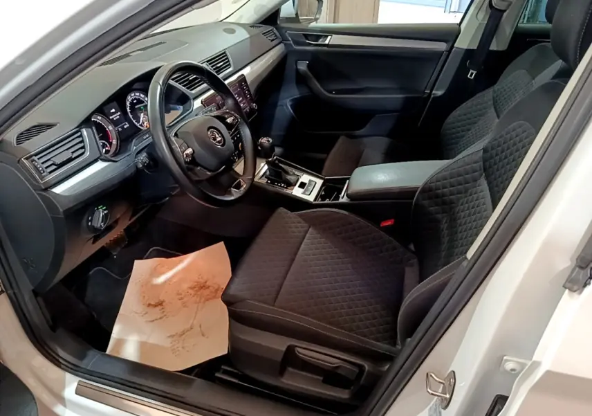 Intérieur côté conducteur d'une Skoda Superb blanc 2021, sièges noirs matelassés et tableau de bord moderne.