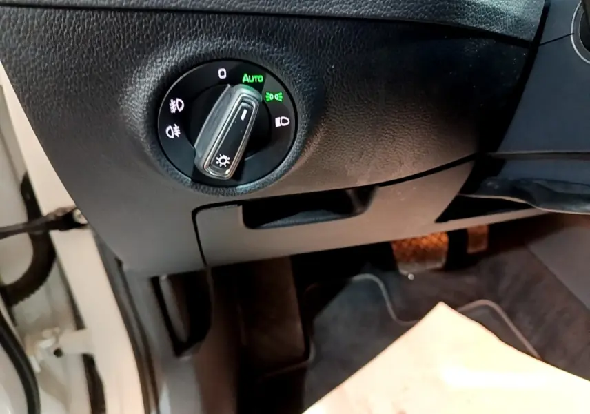Gros plan sur le bouton de commande des phares en position automatique, tableau de bord noir d'une Skoda Superb blanche.