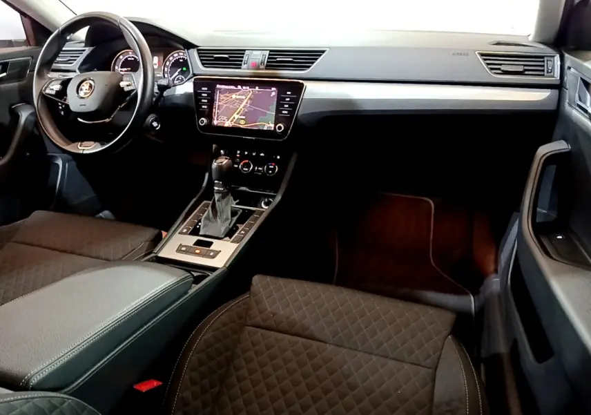 Vue intérieure côté conducteur de la Skoda Superb 2021, tableau de bord noir avec écran tactile et sièges en tissu matelassé.