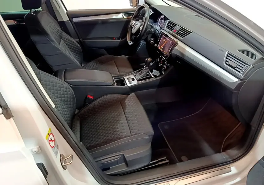 Intérieur côté conducteur d’une Skoda Superb blanche 2021, sièges noirs matelassés et tableau de bord avec écran tactile.