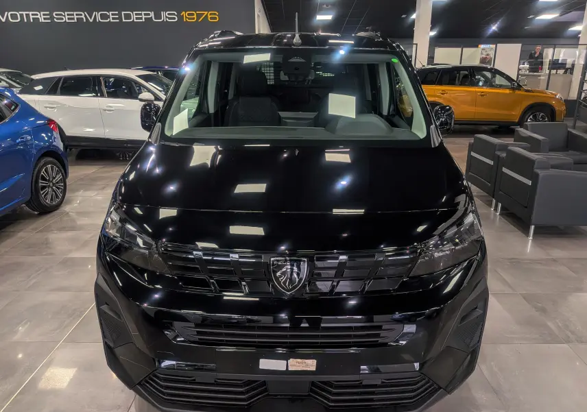 Vue avant d'un Peugeot Rifter noir 2025 en showroom, mettant en valeur sa calandre distinctive et ses optiques modernes.