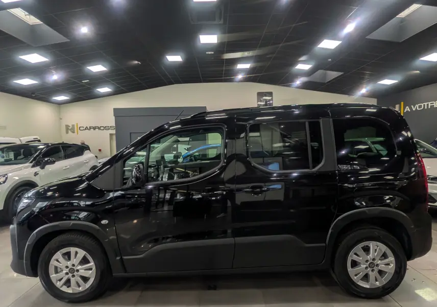 Vue latérale droite d'un Peugeot Rifter noir 2025 en intérieur, avec jantes alliage 16 pouces et vitres teintées.