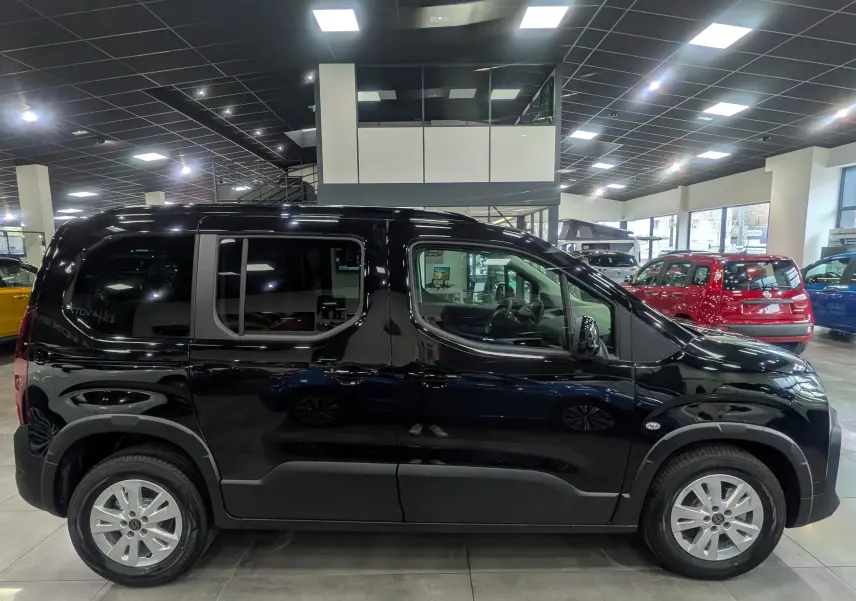 Vue de profil côté gauche d’un Peugeot Rifter noir 2025 en showroom, avec jantes alliage et vitres teintées.